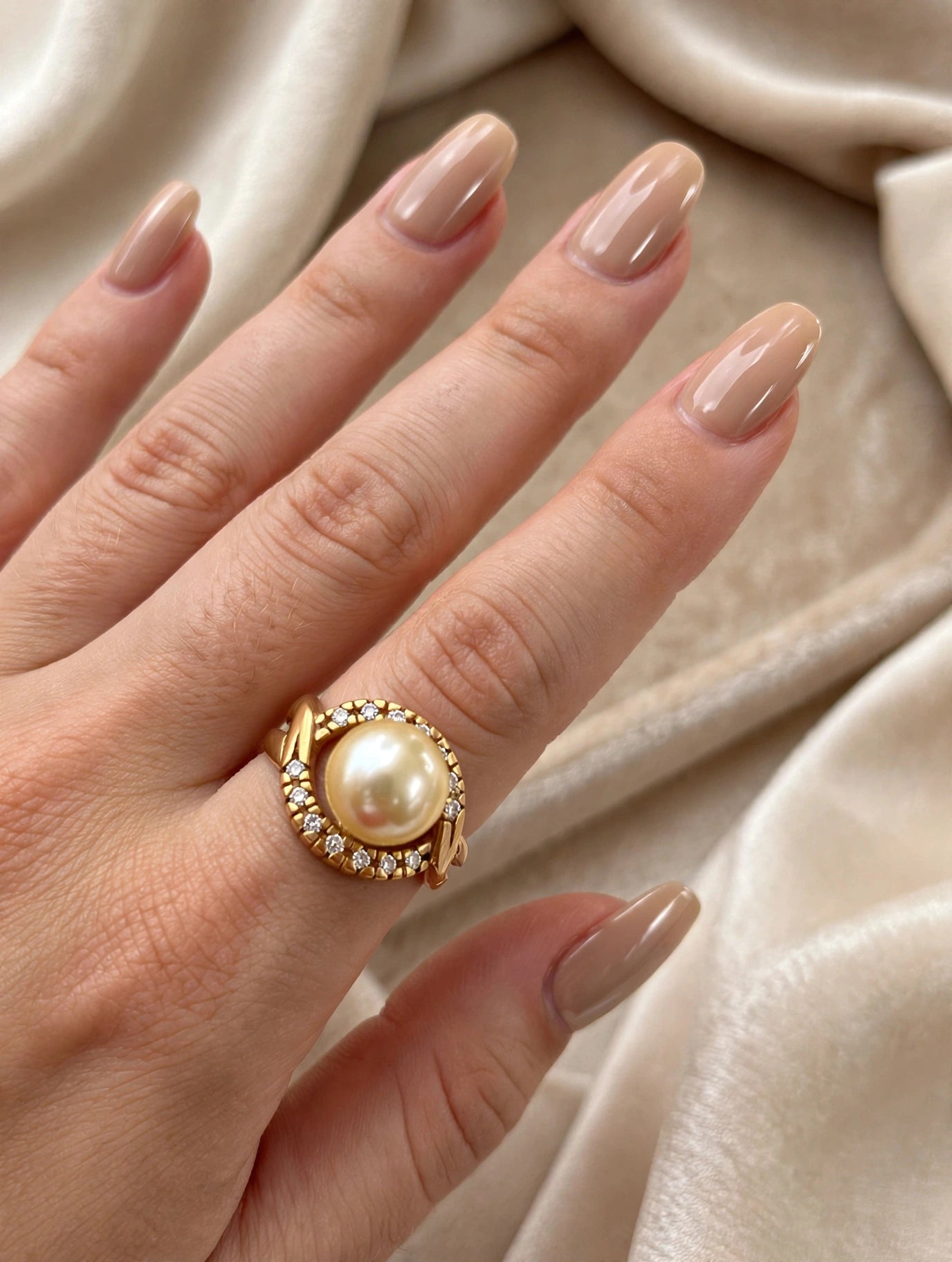 Anel Pérola com Halo de Zircónias Rommanel - no dedo com unhas nude sobre tecido cetim creme